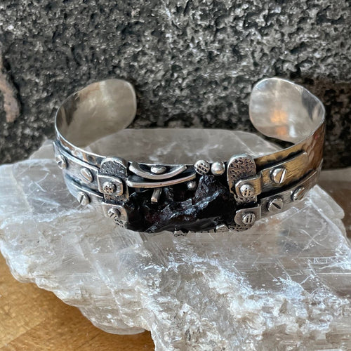 Hammered sterling silver cuff set with Silkote Alin meteorite in an industrial style including textured metal and silver “rivets.”