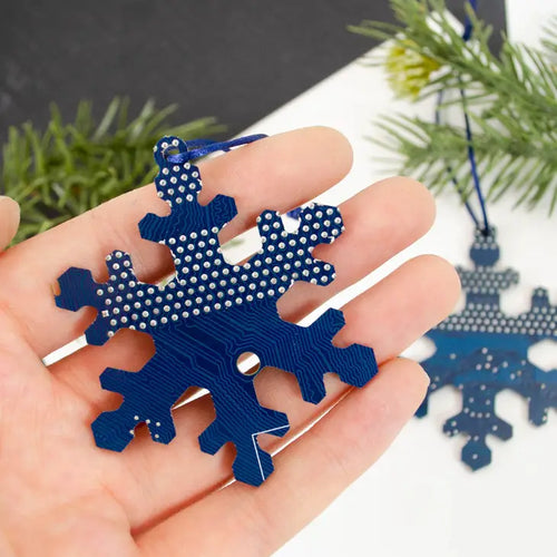 Nerds need holiday decor too! With the aid of a computer controlled routing machine and some programming, blue circuit board was cut into a snowflake shape. The untreated ornament is 2-3/4 inches (7 cm) tall and hangs from a red satin cord. As the circuit boards used to create these ornaments are recycled, some minor imperfections are to be expected 